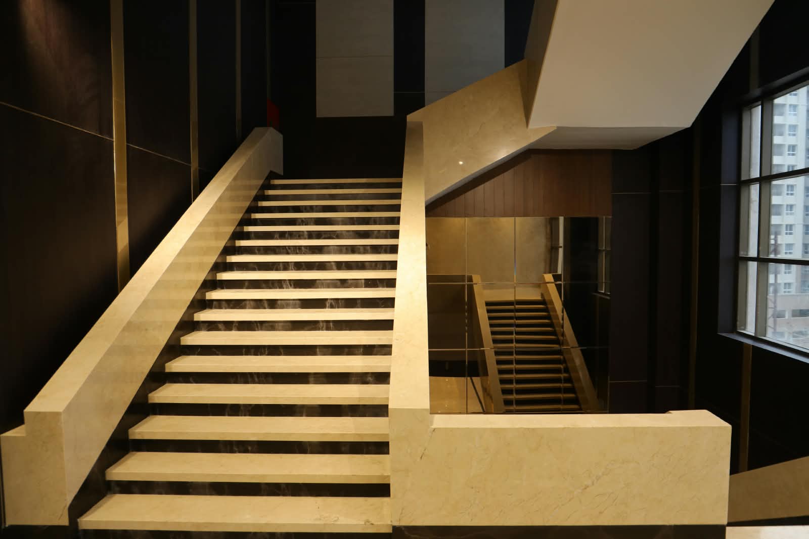 Cream marble staircase with dark stone risers, rising between brass-lined walls