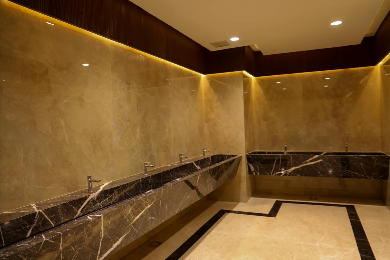Marble washroom with a run of dark stone vanity counters and concealed lighting