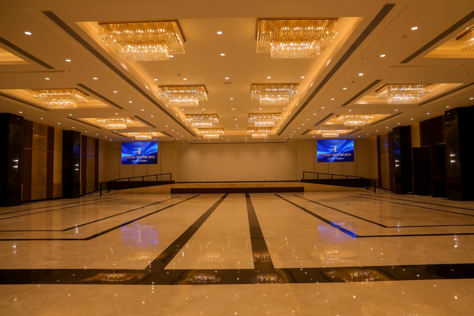 Dominikos hall facing the stage, with rectangular chandeliers stepping back across the ceiling